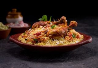 Chicken biriyani using jeera rice arranged in an earthenware with raitha on grey background _ Premium Photo